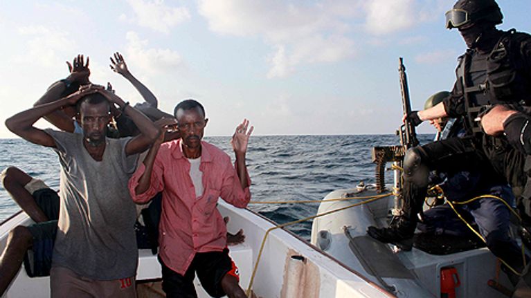 Somalialaisia miehiä veneessä merellä kädet ylhäällä. Vierellä portugalilaisia merisotilaita omassa veneessään taisteluvarustuksessa.