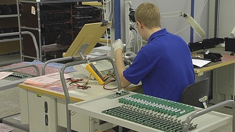 Nuori miestyöntekijä istuu ja työskentelee elektroniikkakomponenttien parissa.