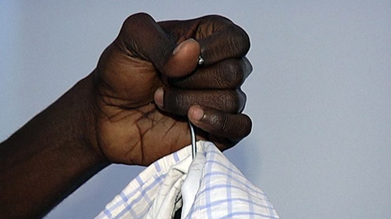Tummaihoinen käsi pitelee vaateripustimesta