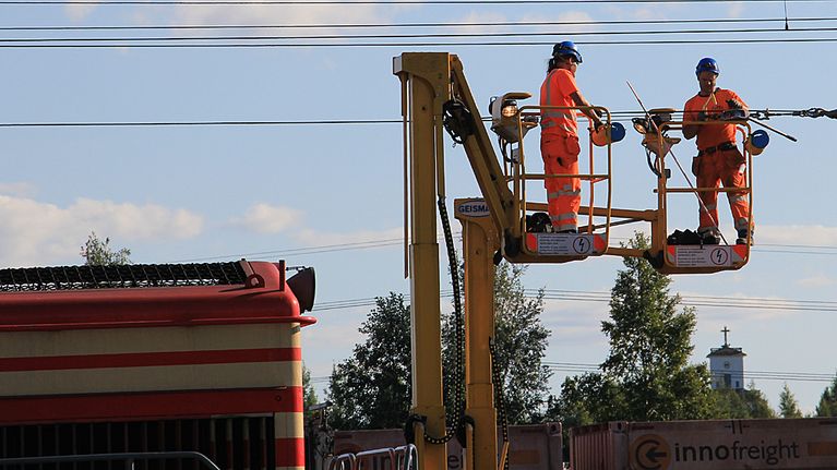 Kuvassa työmiehiä sähköjohtimen kimpussa Kokkolan ratapihalla. 