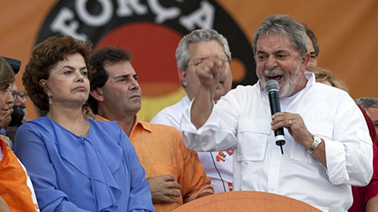 Kuvassa vasemmalla Brasilian entinen presidentti Lula da Silva ja nykyinen presidentti Dilma Roussef. He ovat lavalla. Lula puhuu. 