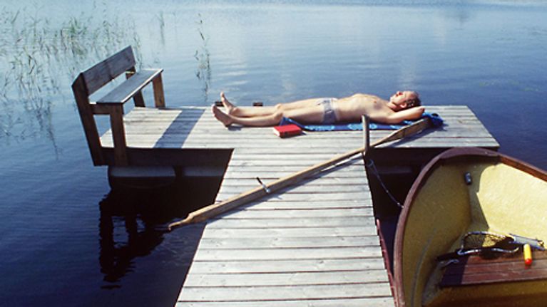 Mies ottaa aurinkoa laiturilla.