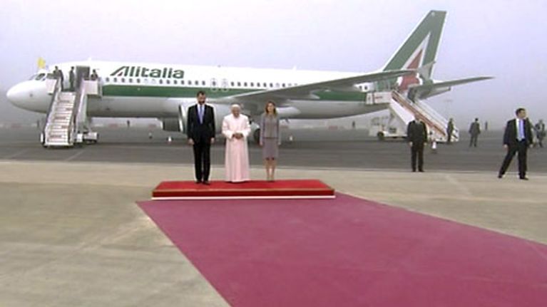 Paavi Asturian prinssin ja prinsessan välissä lentokoneen edessä punaisella matolla..