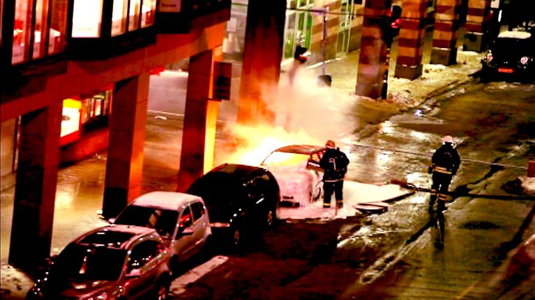 Palomiehet sammuttavat vaahtosammuttimella toista räjähtäneistä autoista Tukholman Drottninggatanilla.