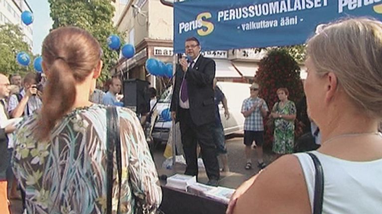 Mies puhuu mikrofoniin lavalla
