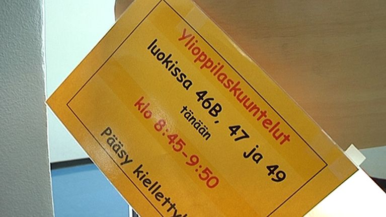 Tuolin selkänojasta riippuva lappu varoittaa ylioppilaskuunteluista.