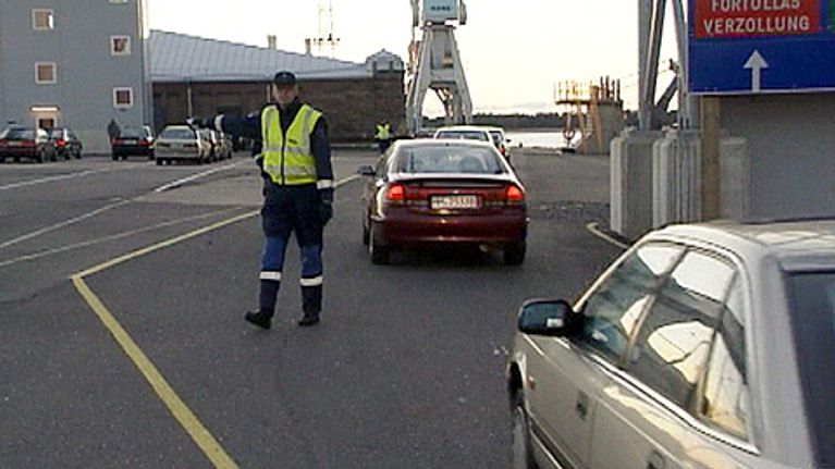 Tullimies ohjaa tuontiautoja satamassa