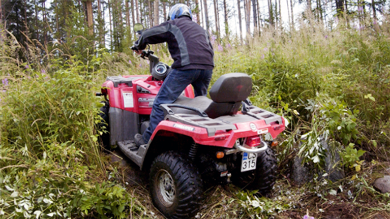 Mies ajaa mönkijällä metsässä.