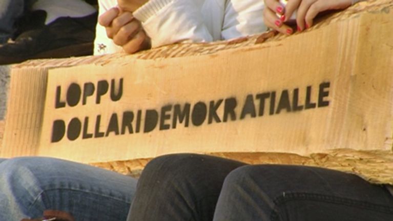 Lankun pätkä, jossa lukee "Loppu dollaridemokratialle" -teksti stencil-tyyliin sumutettuna mustalla spray-maalilla.
