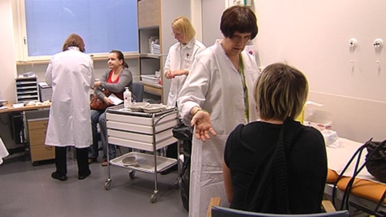 Hoitohenkilökuntaa ja potilaita terveysaseman tai sairaalan tiloissa. Potilaita rokotetaan.
