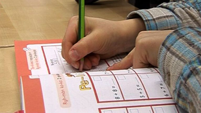 Koululainen laskee laskuja matematiikan kirjaan.