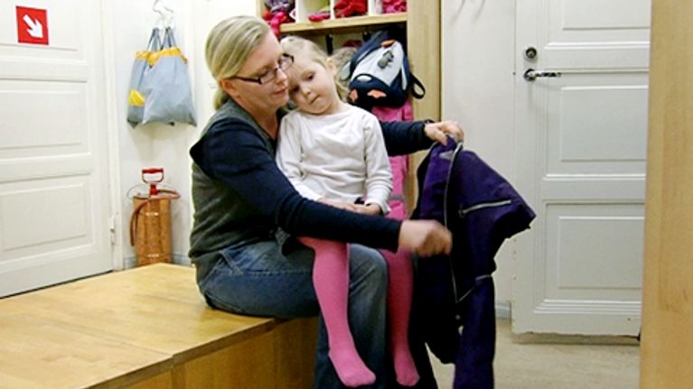 Johanna Jauhiainen pukee haalaria tyttärensä päälle päiväkodin eteisessä.