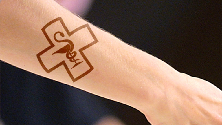 Kuvamanipulaatio: lääketieedettä symboloiva ristin, käärmeen ja pikarin symboli tatuoituna käsivarteen.