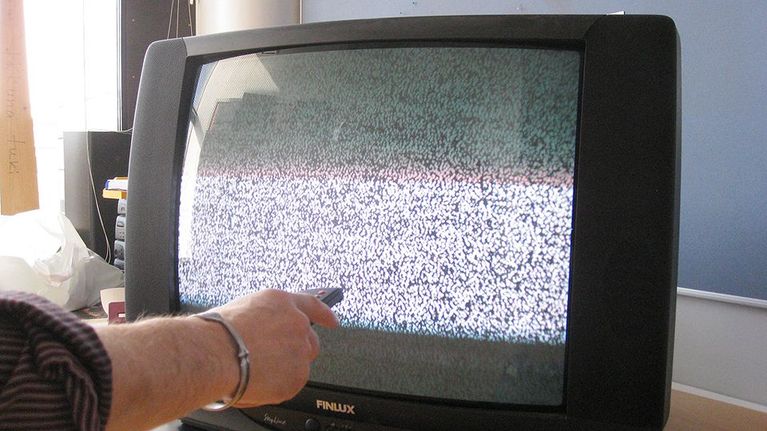 Kuvassa ihminen yrittää kaukosäätimellä televisoon kuvaa lumisateen tilalle.