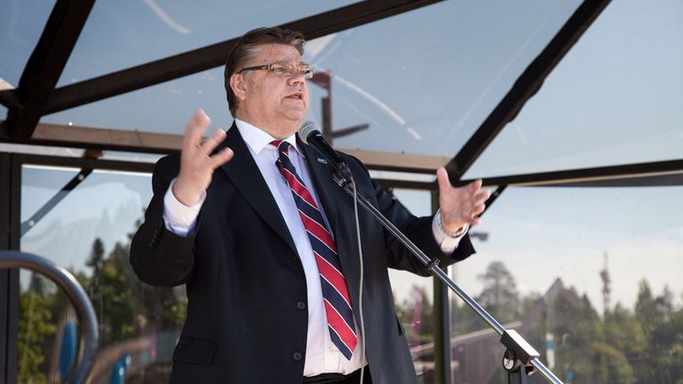 Timo Soini puhuu mikrofoniin elehtien kädet levällään.