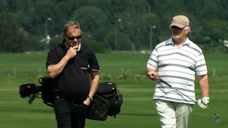 Kaksi miestä kävelee golf-kentällä.