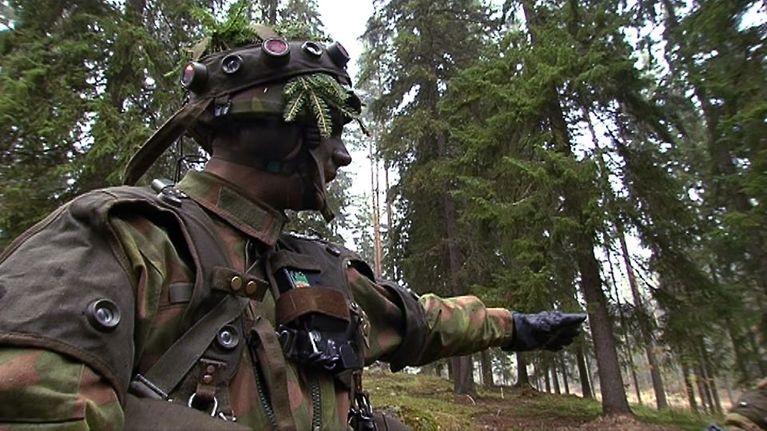 Taisteluvarustukseen sonnustautunut varusmies antaa ohjeita maastossa.