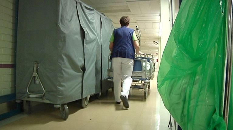 Kuvassa hoitaja työntää potilasvuodetta ahtaalla ja tavaroita täynnä olevalla käytävällä