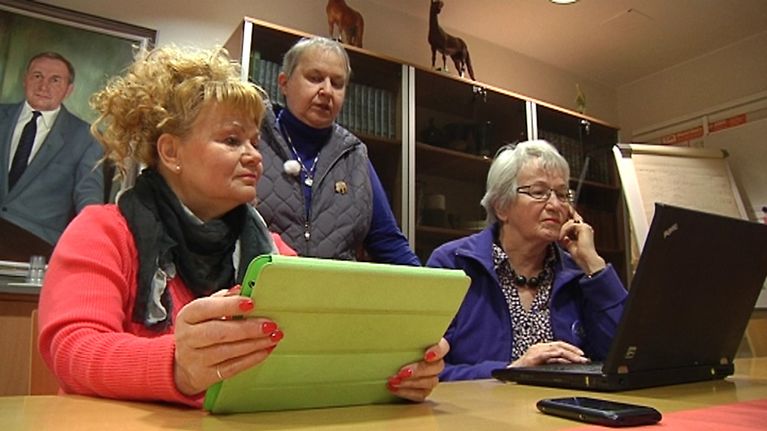 Kuvassa nettimuori Marjatta Laine opastaa Taina Alankoa ja Kaarina Pesolaa netin käyttöön. Alanko ja Pesola istuvat tietokonet edessään ja Laine seisoo heidän takanaan.