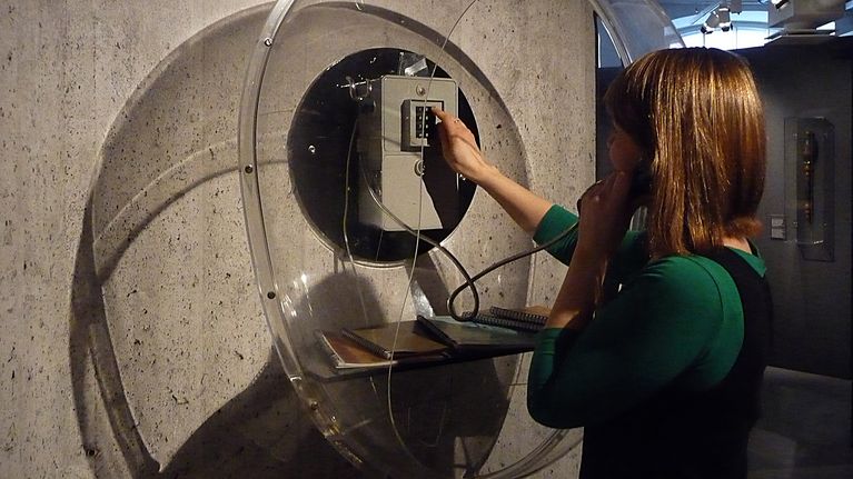 Nainen valitsee numeroa yleisöpuhelimessa Tampereen Rupriikki-museossa