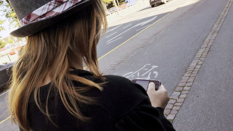 Nuori nainen surffaa kännykällään internetissä kävellessään kadulla.