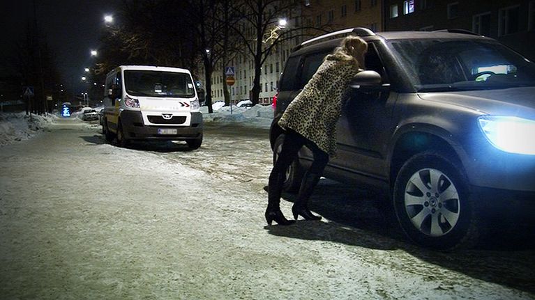 Prostituiotu nainen nojaa autoon.