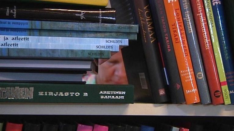 Ihmisen kasvot näkyvät kirjojen takaa.