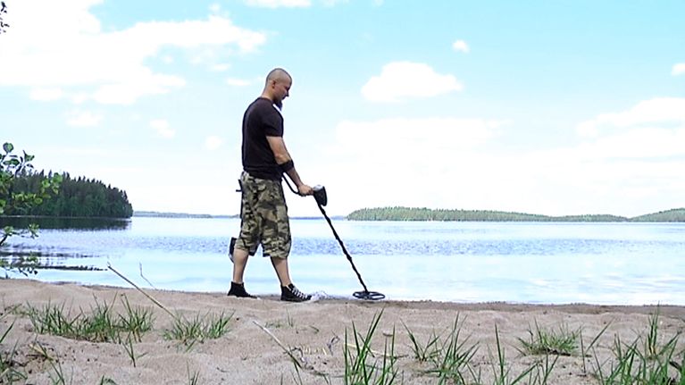 Jarkko Lehtinen haraa metallinpaljastimella rantaa.
