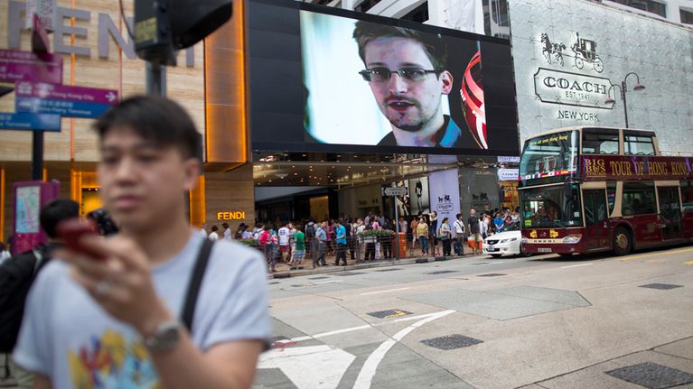 Hongkonglaisessa uutiskatsauksessa pyöritetään Edward Snowdenin arkistokuvaa samaan aikaan, kun paikallinen kadulla kävelijä seuraa oman kännykkänsä näyttöä.