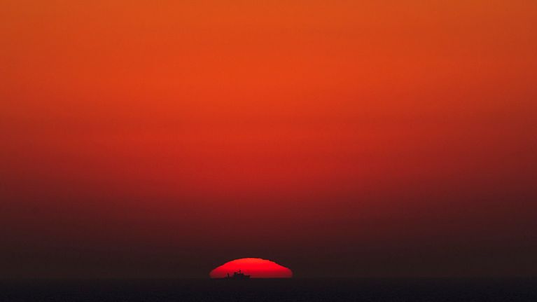 Vene laskevan, punaisen auringon edessä Välimerellä.