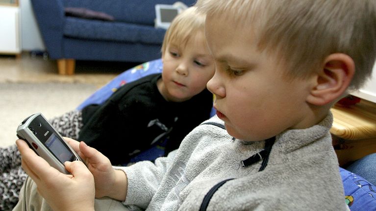 kaksi lasta tutkii kännykkää