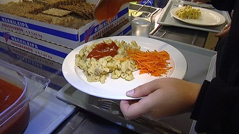 Oppilas annostelemassa ketsuppia makaronilaatikolle kouluruokalassa.