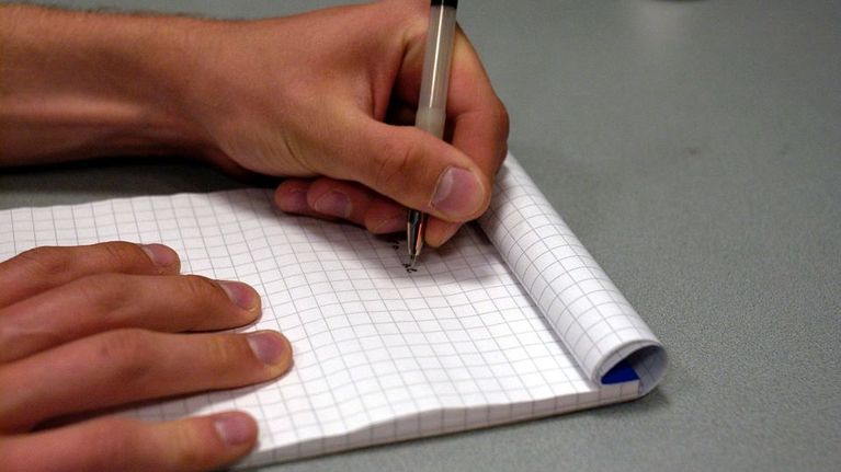 Mies kirjoittaa muistiinpanoja ruutupaperille.