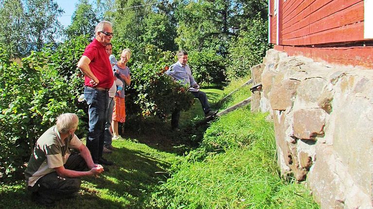 Ihmiset keskustelevat vanhan talon kivijalan juurella.