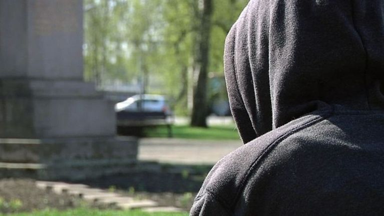 Huppupäinen ihminen istuu puiston penkillä.