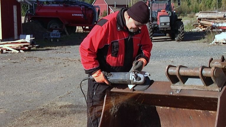 Mies hioo traktorin kauhaa kulmahiomakoneella