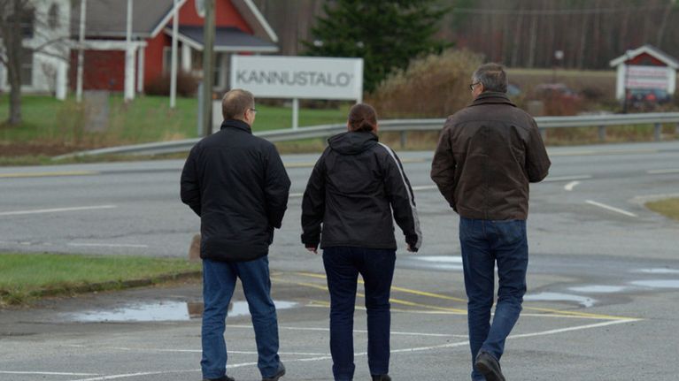 Kolme miestä kävelee poispäin, taustallla Kannustalon kyltti