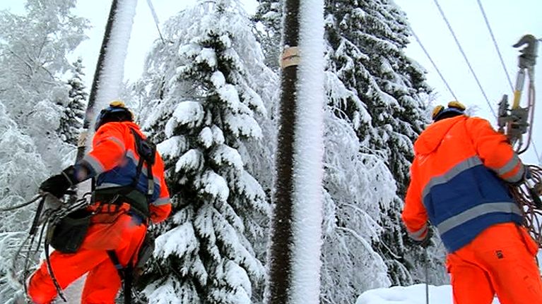 Kaksi sähkömiestä korjaa lumisessa metsässä kaapelia