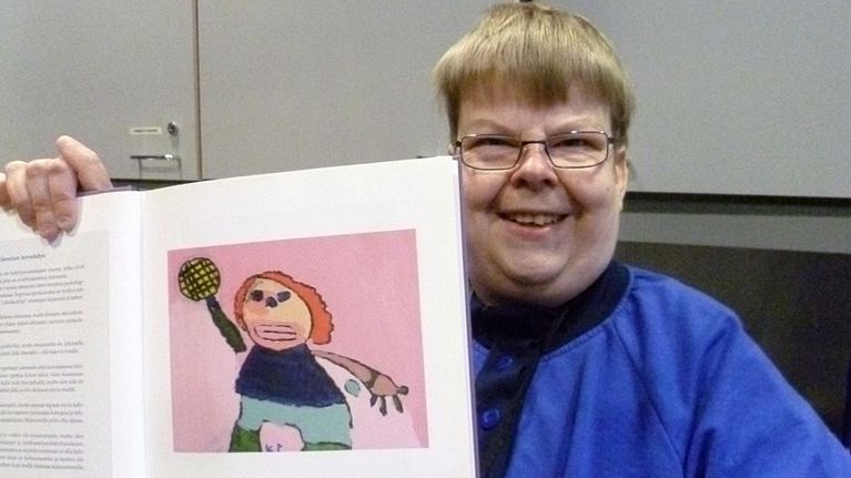 Kimmo Tolvanen näyttää kirjan sivulta maalaustaan