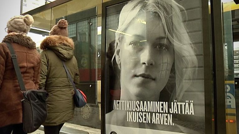 Ihmiset kävelevät nettikiusaamisesta kertovan mainoksen ohi.