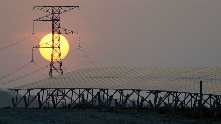 Aurinko näkyy voimalinjan takana.