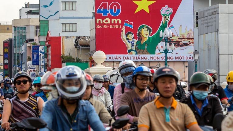 Ihmiset ajavat Vietnamin sodan päättymistä 40-vuotta sitten juhlistavan kyltin ohi Ho Chi Minhissa.