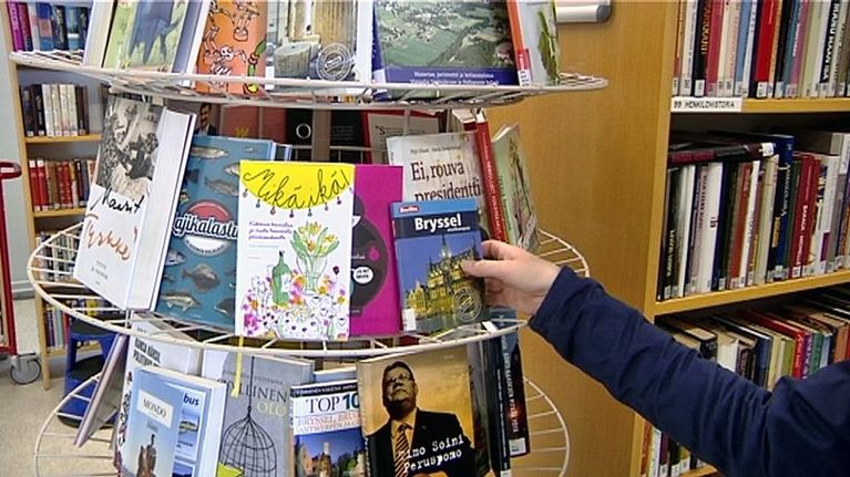 Henkilö ottaa kirjaa kirjaston hyllystä.