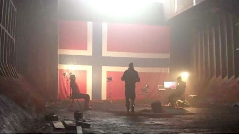 Kolme ihmistä pimeässä bunkkerissa, taustalla suuri Norjan lippu. 