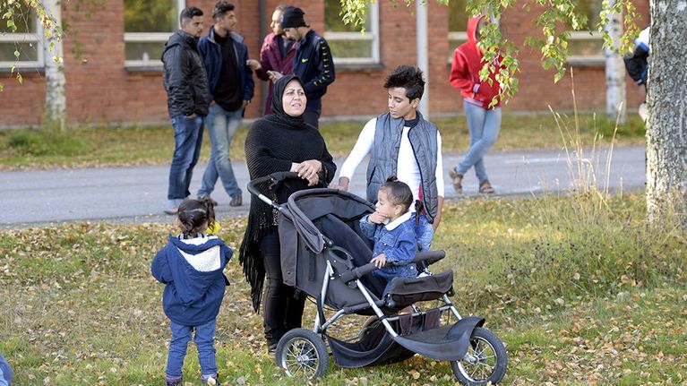äiti kolmen lapsensa kanssa ja kauempana viisi miestä