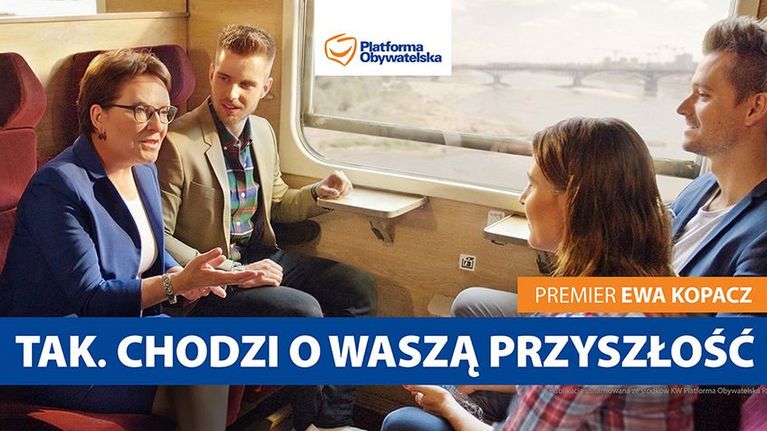 Perhe matkustaa junassa ja pääministeri Ewa Kopacz juttelee heidän kanssaan.