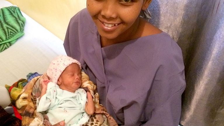 somaliopiskelija hymyilee vastasyntynyt vauva sylissään.
