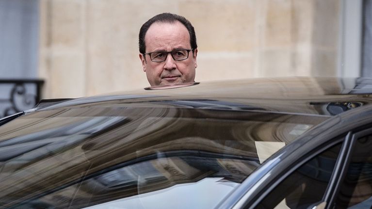 Ranskan presidentti François Hollande nousee autoon Élysée-palatsin edessä. Musta auto on kuvassa etualalla, vain Hollanden pää näkyy auton katon yli. Presidentin ilme on vakava. Taustalla näkyy Élysée-palatsin seinää.