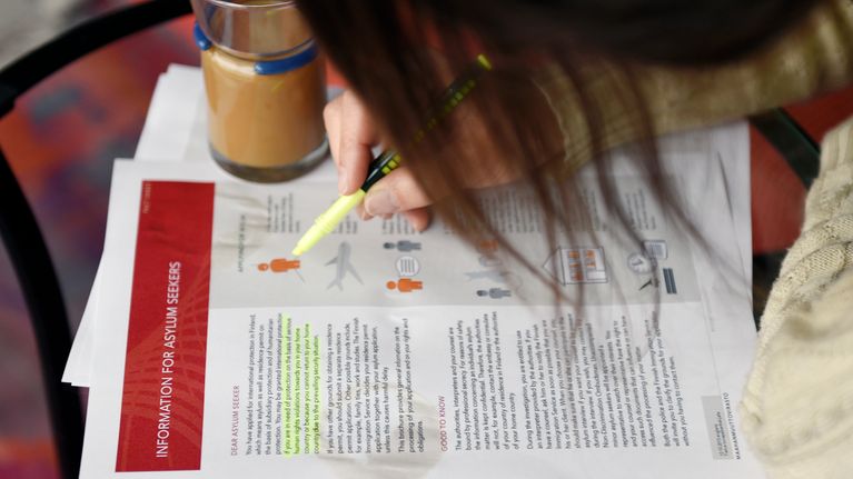 Nainen tutkii maahanmuuttoviraston infopakettia liittyen turvapaikan hakemiseen Suomesta.