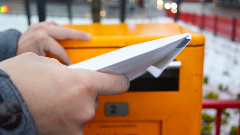 Ihminen työntää kirjekuorta postin laatikkoon.